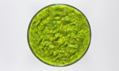 Green guacamole in a glass bowl on a white background